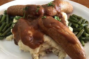 Sausage and mash potatoes with gravy, served with green beans. This is called Bangers 'N' Mash.